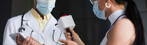 cropped view of reporter in medical mask holding microphone near doctor in white coat with digital tablet, banner