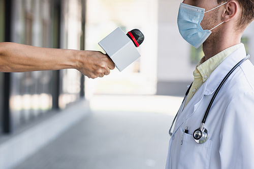cropped view of reporter holding microphone near doctor in medical mask