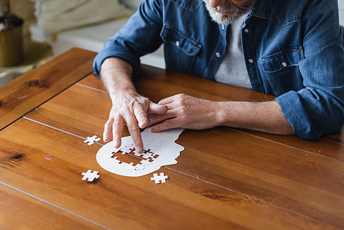 Cropped view of elderly man with alzheimer folding puzzle