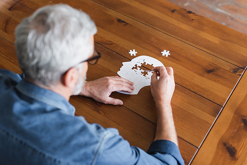 Overhead view of senior man on blurred foreground folding puzzle on table