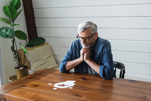 Pensive senior man looking at jigsaw on table