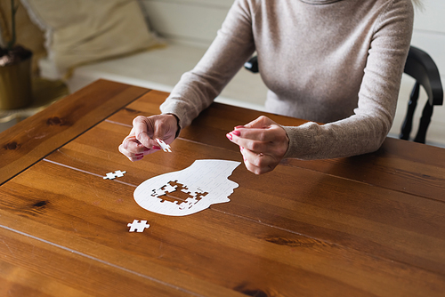Cropped view of senior woman holding puzzle near table