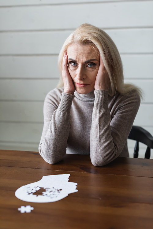 Sad senior woman with dementia  near jigsaw on blurred foreground