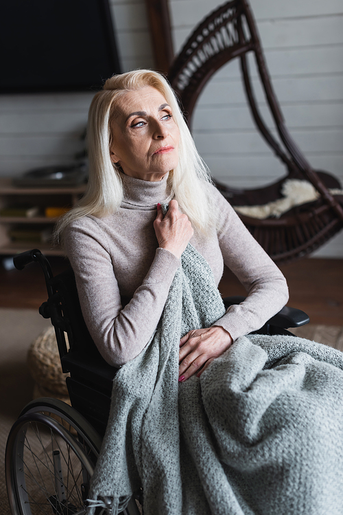 Lonely woman holding blanket on armchair at home