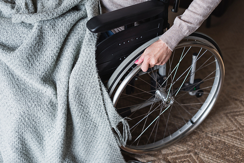 Cropped view of elderly woman holding wheel of wheelchair at home