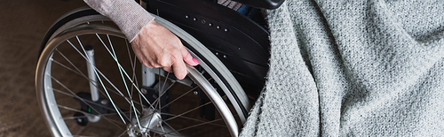 Cropped view of elderly woman with blanket holding wheel of wheelchair, banner