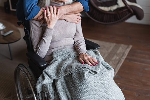 cropped view of senior man hugging disabled wife in .