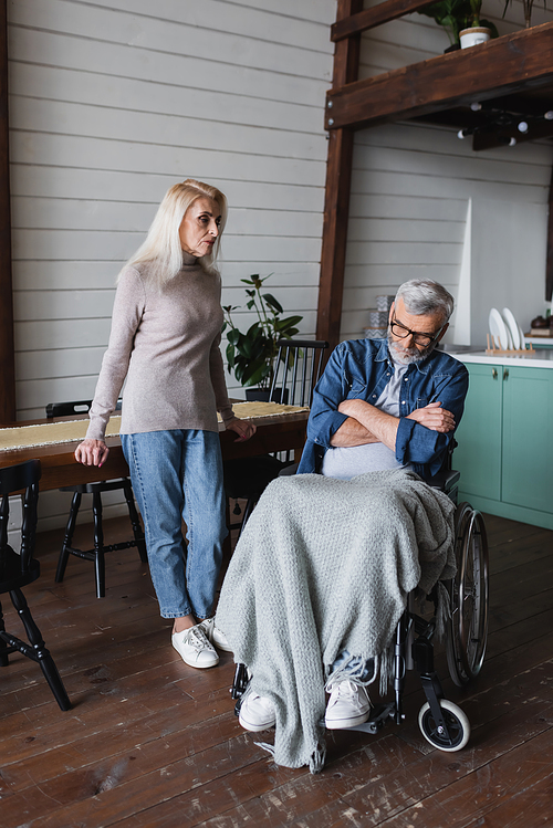 Woman looking at disabled husband with crossed arms at home