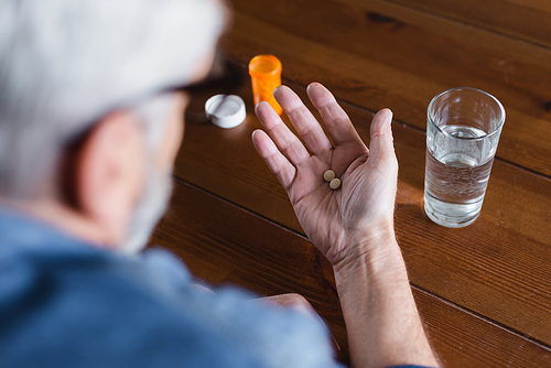 Blurred man holding pills on hand near jar and glass of water