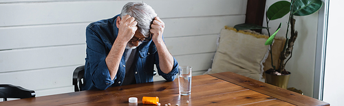 Depressed man looking at pills near glass of water, banner