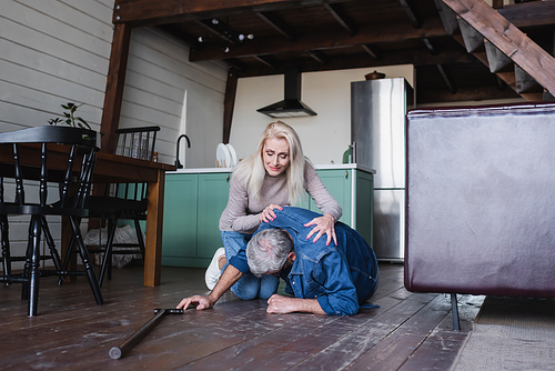 Worried woman hugging senior husband with crutch on floor