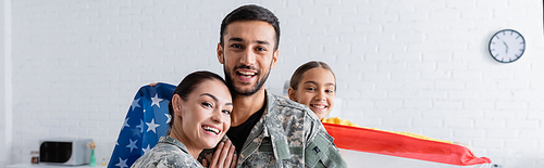Smiling parents in military uniform  near child with american flag at home, banner