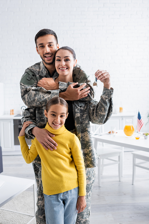 Smiling man in military uniform hugging wife with key near child at home