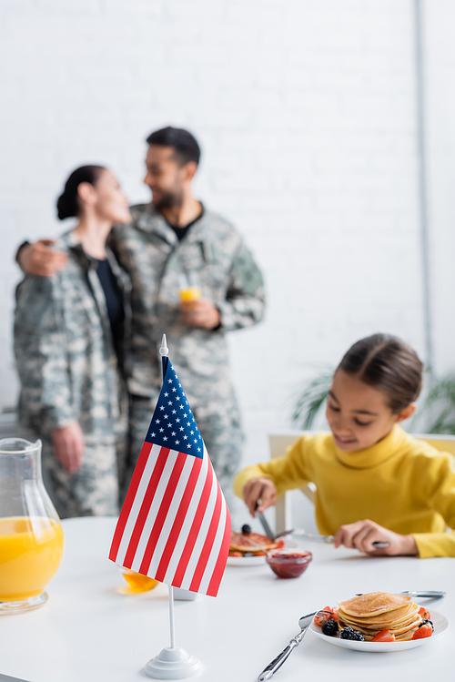 American flag near child with breakfast and parents in military uniform on blurred background