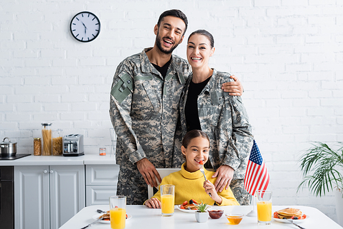Parents in military uniform  near child, breakfast and american flag in kitchen