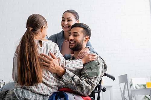 Man in military uniform and wheelchair with american flag smiling at daughter near wife at home
