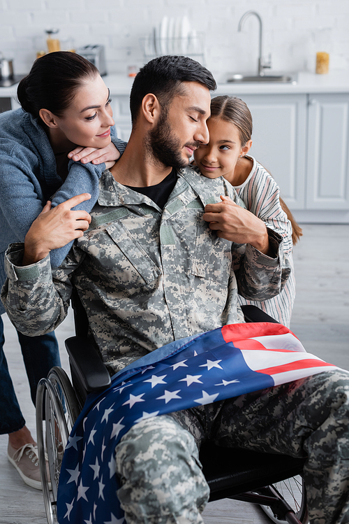 Soldier in wheelchair with american flag near daughter and wife at home