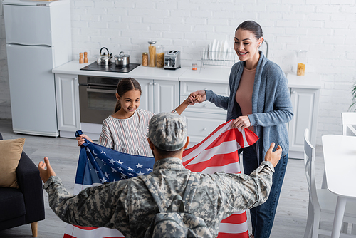Smiling family holding american flag near soldier at home