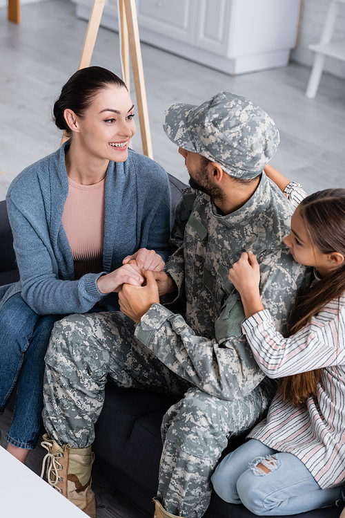 High angle view of woman holding hands of husband in military uniform near child on couch