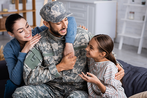 Positive family sitting near man in military uniform on couch