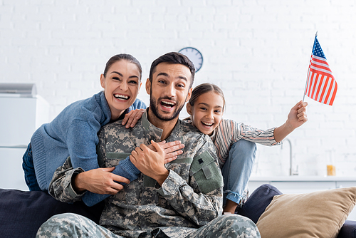Positive family with american flag  near man in military uniform at home