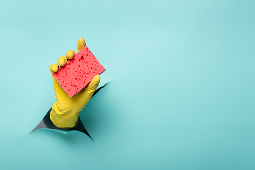 partial view of cleaner in rubber glove holding sponge through hole in paper wall on blue