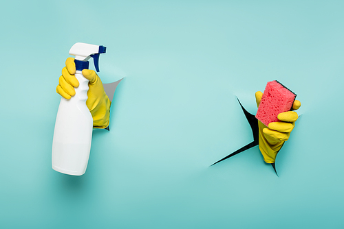 partial view of cleaner in rubber gloves holding sponge and spray bottle through holes in paper wall on blue
