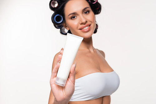 smiling young woman in curlers and top showing cream tube and  isolated on white