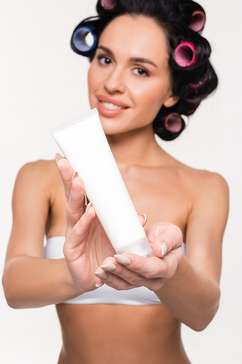 cream tube in hands of blurred smiling young woman in curlers isolated on white