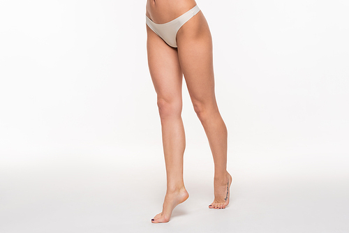 partial view of young woman in beige panties and with fit legs standing on tiptoes on white