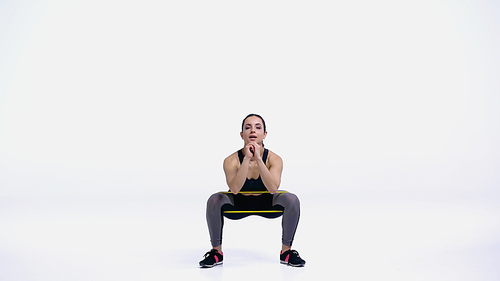 brunette young sportswoman doing squat with yellow elastics on white