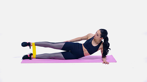 brunette young sportswoman working out with elastics on pink fitness mat on white