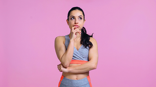 pensive young woman in sportswear looking away isolated on pink