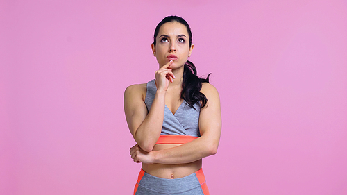 thoughtful young woman in sportswear looking away isolated on pink