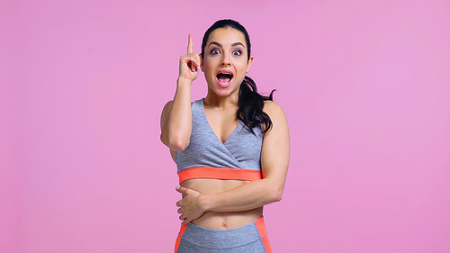 excited young woman in sportswear pointing with finger isolated on pink