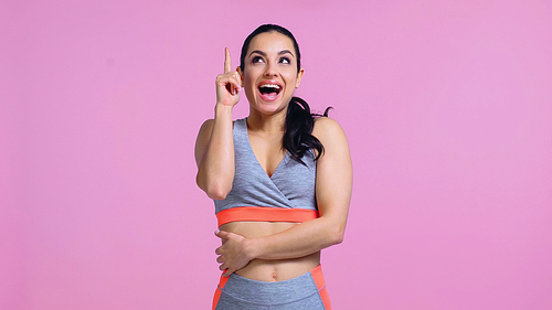 amazed young woman in sportswear pointing with finger and looking up isolated on pink