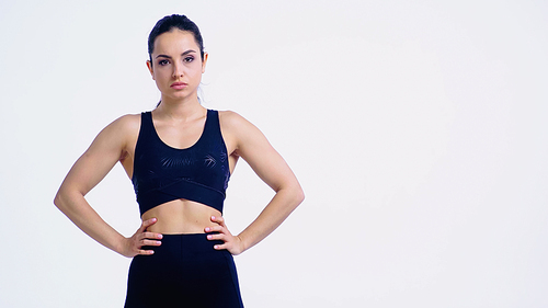 displeased young woman in sportswear standing with hands on hips isolated on white