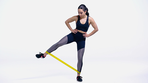 full length of young woman in sportswear exercising with resistance band on white