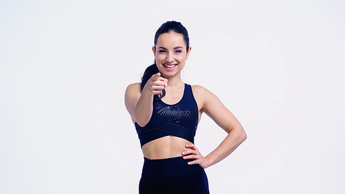 smiling sportswoman pointing with finger while standing with hand on hip isolated on white