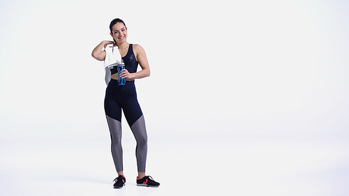 happy sportswoman with towel and sports bottle standing on white