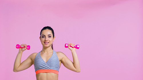 cheerful woman working out with dumbbells isolated on pink