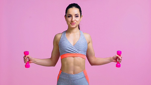 pleased young woman working out with dumbbells isolated on pink