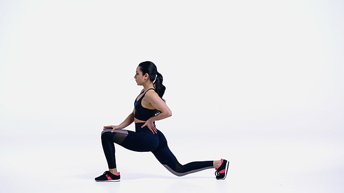 flexible young woman in sportswear doing lunges on white