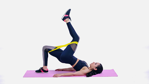 brunette young sportswoman exercising with elastics on pink fitness mat on white