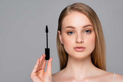 young woman holding brush with black mascara isolated on grey