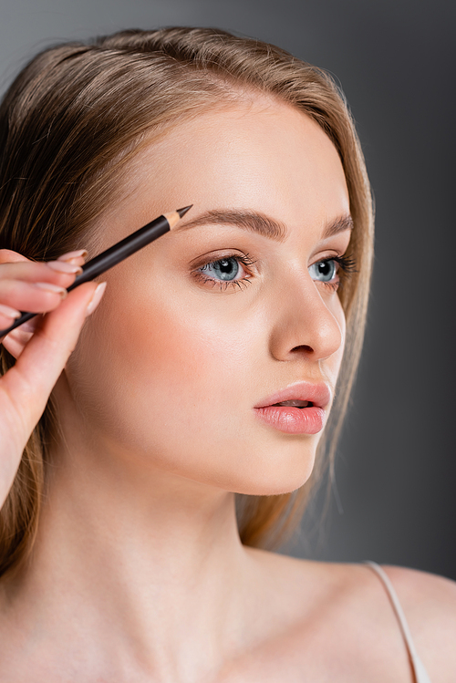 young woman applying brown eyebrow 펜슬 isolated on grey