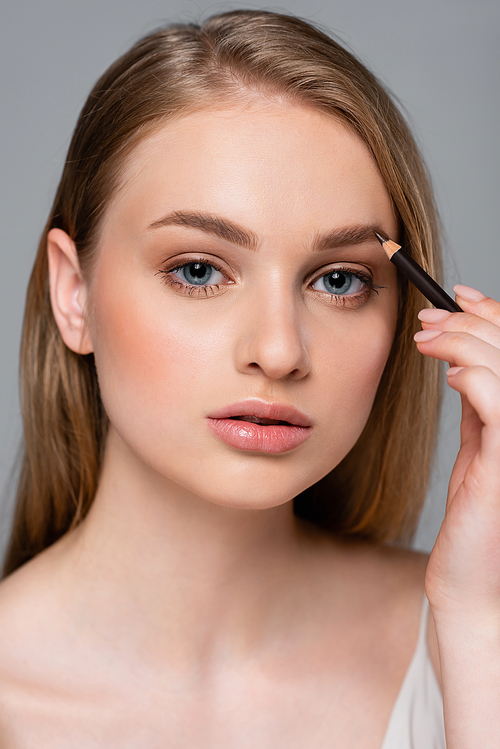 young woman with lip gloss applying brown eyebrow 펜슬 isolated on grey