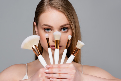 young woman holding set of different cosmetic brushes isolated on grey