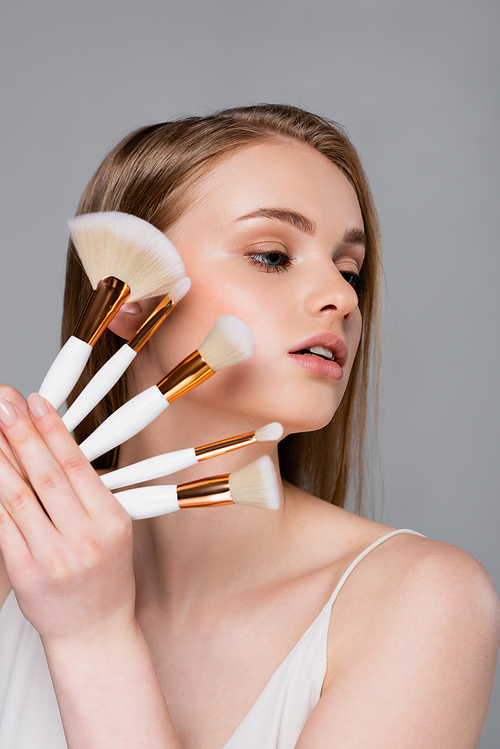 young woman holding set of different cosmetic brushes isolated on gray