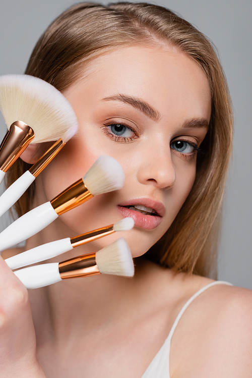 young woman holding set of different cosmetic brushes while  isolated on grey